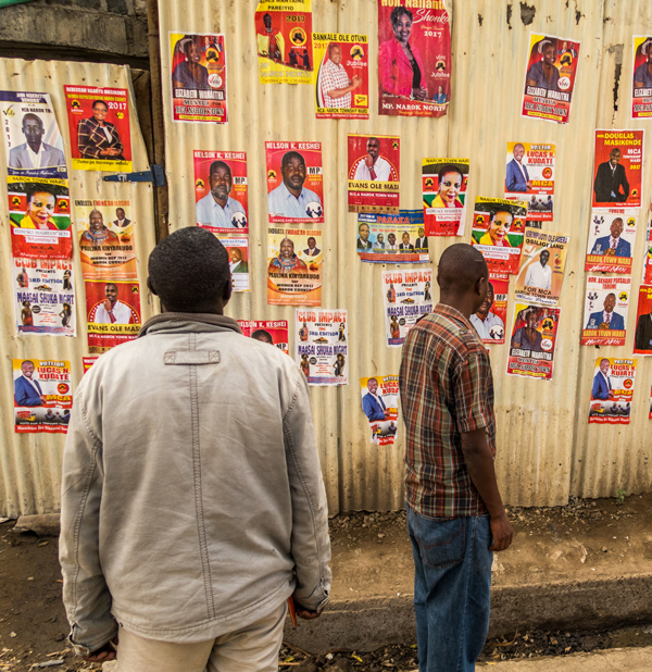 People walking past a wall of election campaign posters in Narok County, Kenya in the run-up to the national elections in August 2017. (Stephen Butler / Shutterstock)